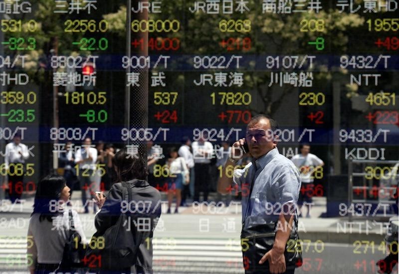 © Reuters. Tokyo, davanti al tabellone elettronico di un brokerage con gli andamenti dei titoli di borsa