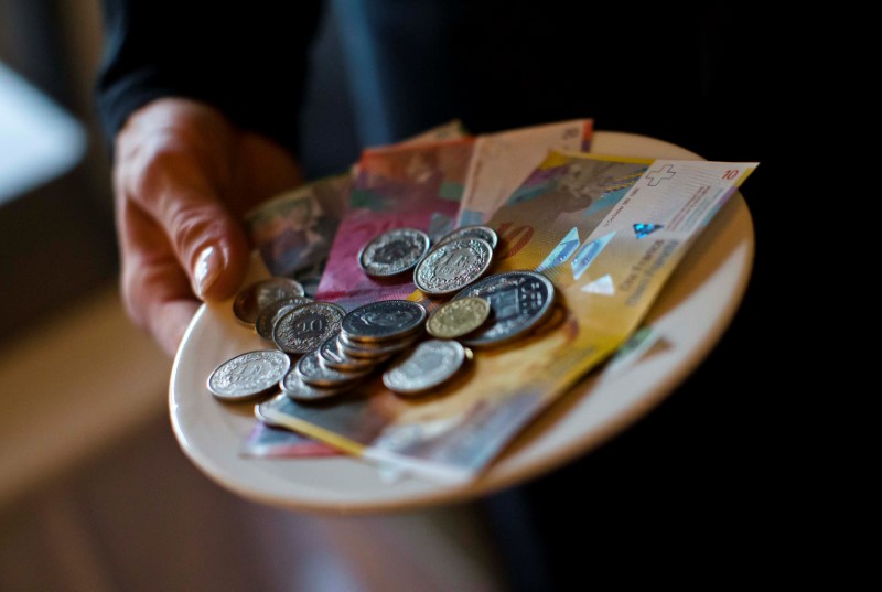 © Reuters. A waitress presents a plate with various Swiss Franc coins and notes in this picture illustration in a restaurant in Zurich