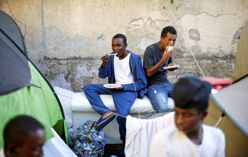 © Reuters. Migrants eat after getting food from volunteers at a makeshift camp in Via Cupa (Gloomy Street) in downtown Rome