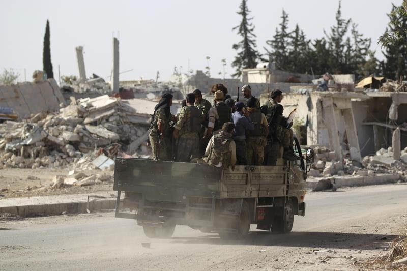 © Reuters. Rebel fighters drive past damaged buildings in al-Rai town, northern Aleppo countryside
