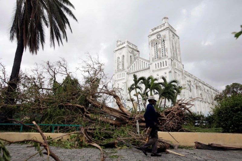 © Reuters. A man carrying branches from fallen trees walks next to the Cathedral after Hurricane Matthew in Les Cayes