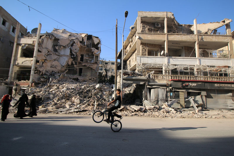 © Reuters. A boy plays with a bicycle past damaged buildings in the rebel held Seif al-Dawla neighbourhood of Aleppo