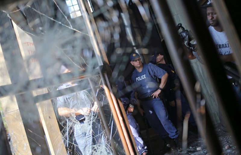 © Reuters. A police officer looks on at a damaged window after students clashed with security at Johannesburg's University of the Witwatersrand as countrywide protests demanding free tertiary education entered a third week, South Africa