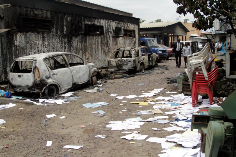 © Reuters. Congolese civilians walk past a house and vehicles which were burnt during anti-government protests to press President Joseph Kabila to step down in the Democratic Republic of Congo's capital Kinshasa