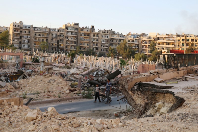 © Reuters. People walk near an over-crowded graveyard in the rebel held al-Shaar neighbourhood of Aleppo