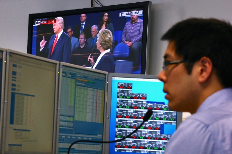 © Reuters. A trader works at his desk as the US presidential town hall debate is shown on television at Citibank's trading floor located in central Sydney, Australia
