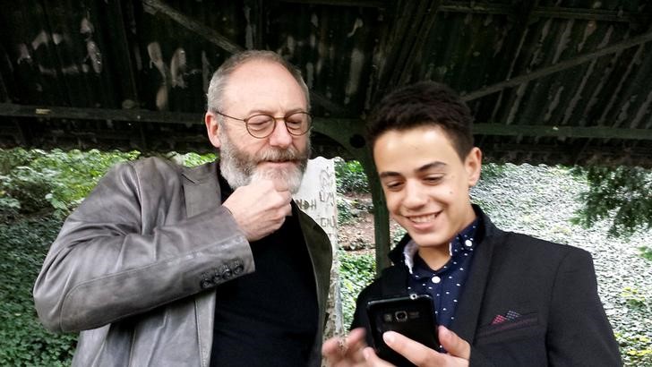 © Reuters. Ator Liam Cunningham sorri durante visita a refugiado sírio Hussam em Stuttgart