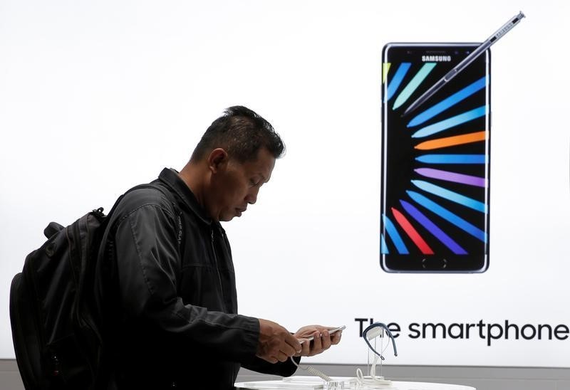 © Reuters. A customer holds a smartphone in front of Galaxy Note 7 advertisement at Samsung store in Jakarta