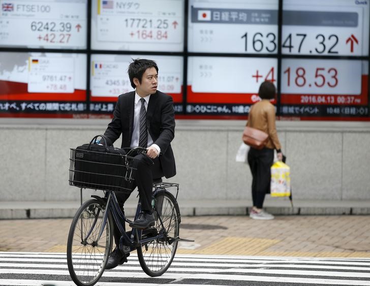© Reuters. A man cycles in front of an electronic board showing Japan's Nikkei average (R) outside a brokerage in Tokyo