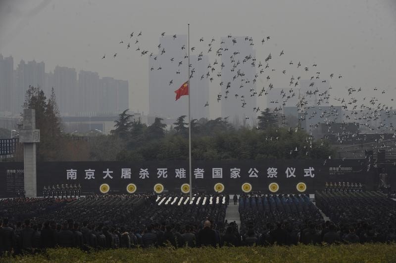 © Reuters. Pigeons fly above a Chinese flag flown at half-staff as people attend a ceremony to mark the second national memorial day for the Nanjing Massacre, at the Nanjing Massacre Museum in Nanjing