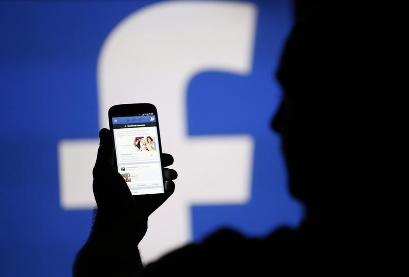 © Reuters. A man is silhouetted against a video screen with an Facebook logo as he poses with an Samsung S4 smartphone in this photo illustration taken in the central Bosnian town of Zenica