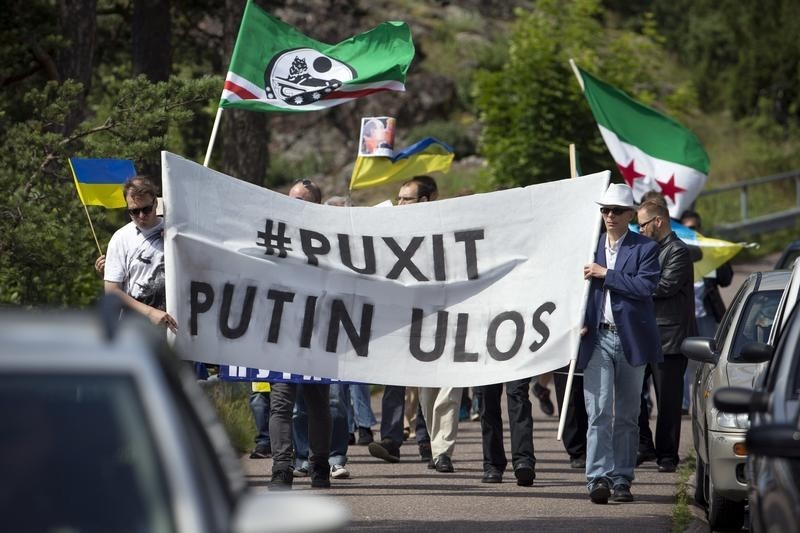 © Reuters. Demonstrators hold a placard reading "Puxit - Putin out" during the visit of Russia's President Vladimir Putin in Naantali