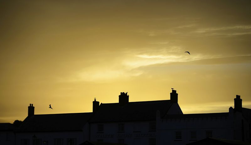 © Reuters. Birds fly over terraced houses as the sun sets over Aldeburgh