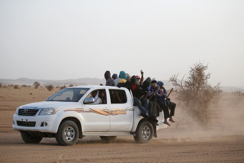 © Reuters. Migrants crossing the Sahara desert into Libya ride on the back of a pickup truck outside Agadez