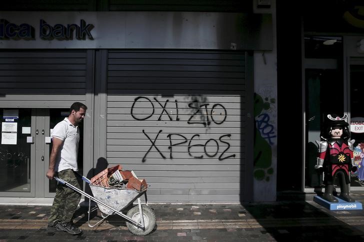 © Reuters. File photo shows graffiti on a closed Attica Bank branch reading "No to the debt" as a worker pushing a cart walks by in Athens