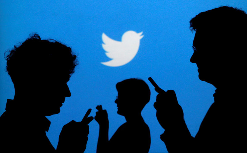 © Reuters. People holding mobile phones are silhouetted against a backdrop projected with the Twitter logo