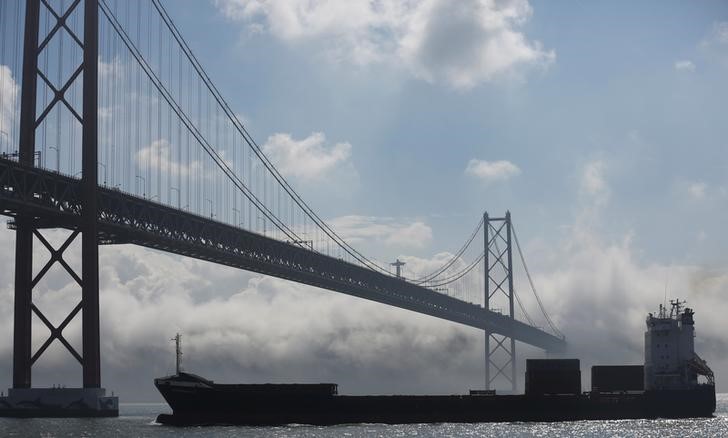 © Reuters. A container ship sails next to April 25 bridge in Lisbon