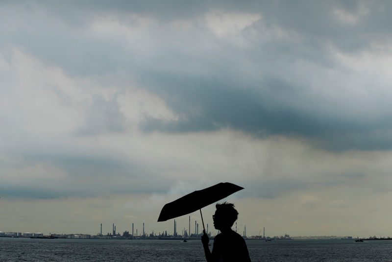 © Reuters. A man carrying an umbrella passes as storm clouds gather over Shell's Pulau Bukom oil refinery in Singapore