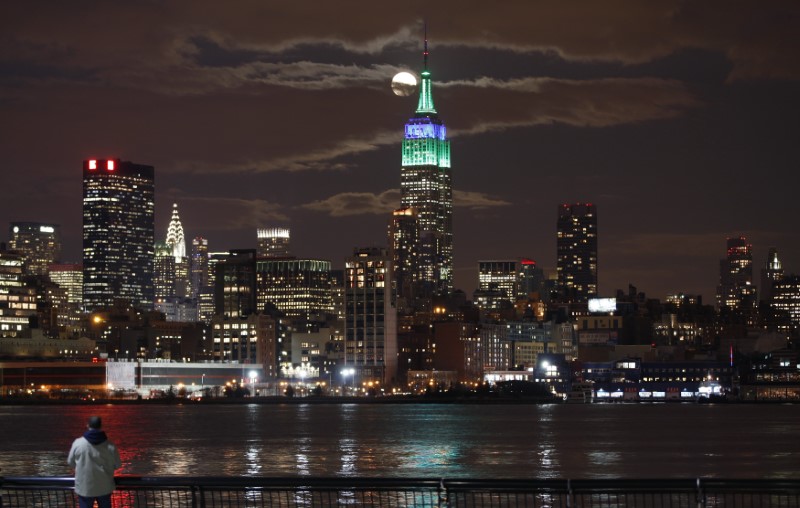 © Reuters. A full moon rises behind the Empire State Building in New York as a man watches in a park along the Hudson River in Hoboken, New Jersey