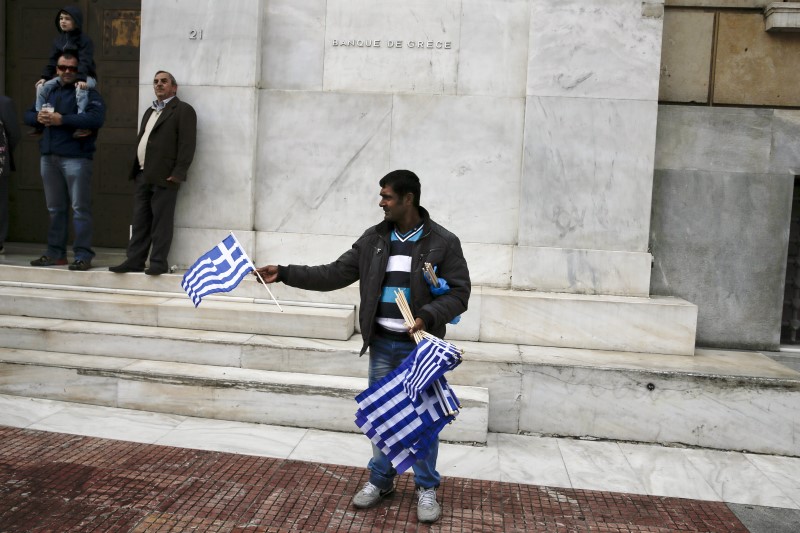 © Reuters. Street vendor displays Greek national flags for sale in front of the Bank of Greece headquarters during a student parade marking the "Ohi" (No) day