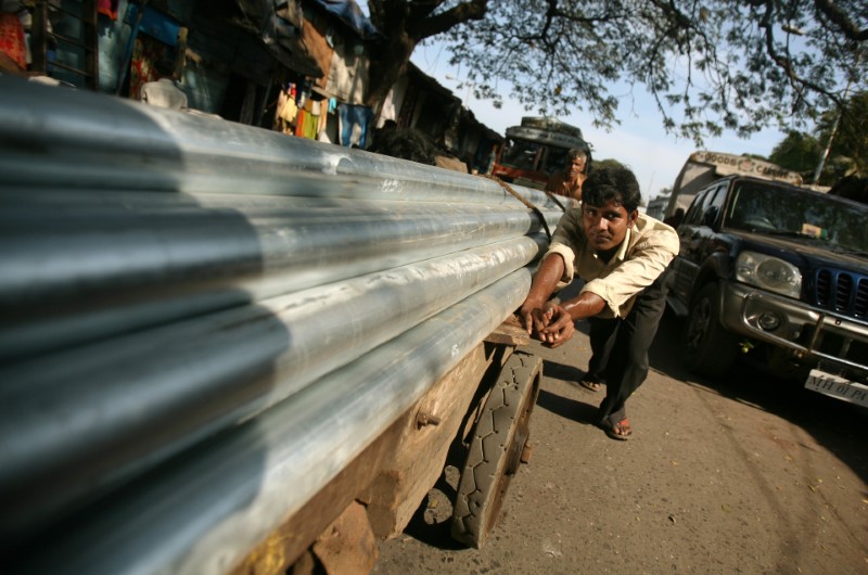 © Reuters. Workers push a cart laden with steel pipes in Mumbai