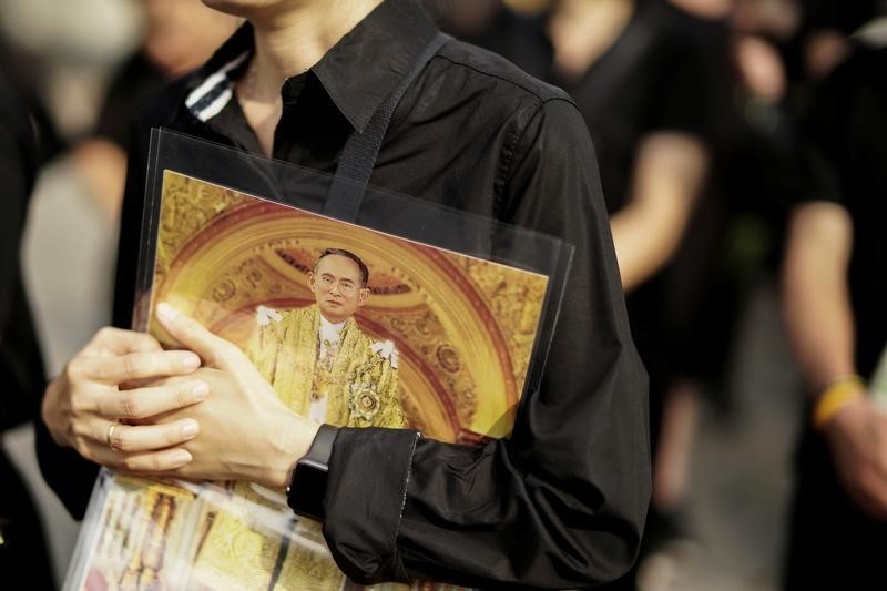 © Reuters. A mourner holds up a picture of Thailand's late King Bhumibol Adulyadej as she waits in line to offer condolences at the Grand Palace in Bangkok