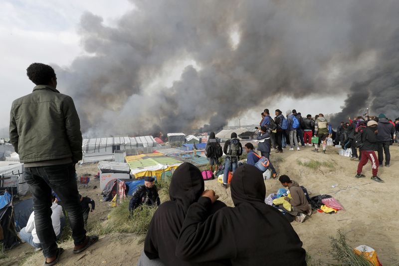 © Reuters. Imigrantes olhando abrigos incendiados no acampamento de Calais