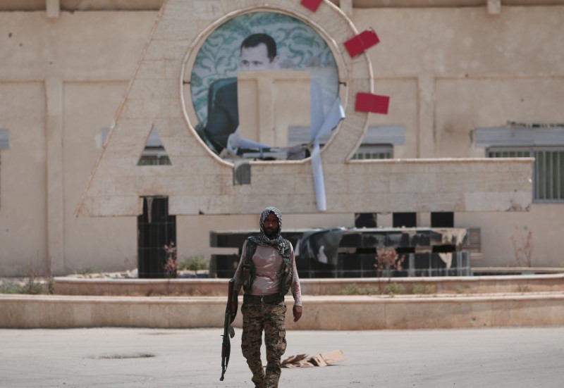 © Reuters. A Kurdish fighter from the People's Protection Units (YPG) carries his weapon as he walks at the faculty of economics where a defaced picture of Syrian President Bashar al-Assad is seen in the background, in the Ghwairan neighborhood of Hasaka