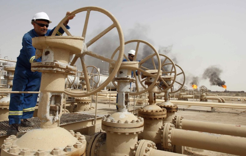 © Reuters. Workers adjust the valves of an oil pipe as smoke rises from burning excess gas in Zubair oilfield in Basra
