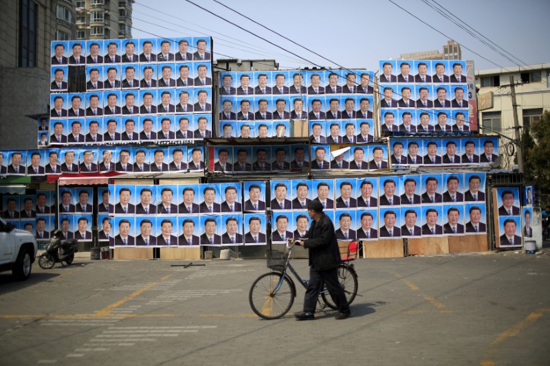 © Reuters. A man with a bicycle walks past a building covered in posters of Chinese President Xi Jinping in Shanghai