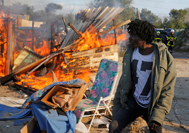 © Reuters. Imigrante em frente abrigo incendiado em protesto no acampamento de Calais, na França