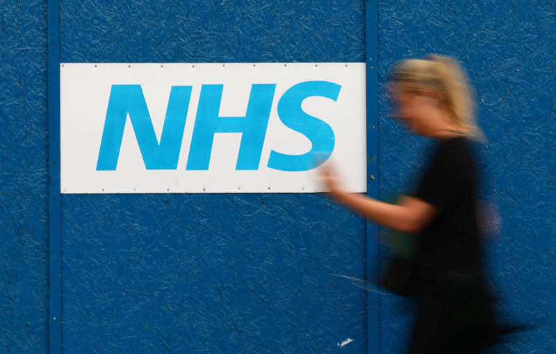 © Reuters. Mulher passa por logo do Serviço Nacional de Saúde (NHS) do Reino Unido, no hospital Royal London, em Londres