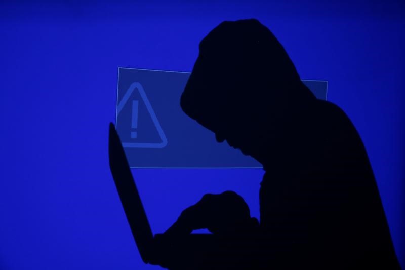 © Reuters. Foto ilustrativa mostra homem de capuz digitando em laptop, em frente a uma tela azul com ponto de exclamação