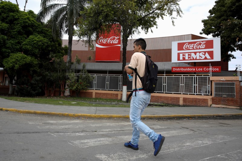 © Reuters. A man walks next to corporate logos of Coca-Cola and Femsa at a distribution center of the company in Caracas
