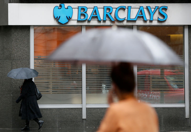 © Reuters. FILE PHOTO: Pedestrians shelter under umbrellas as they walk past a Barclays branch in central London