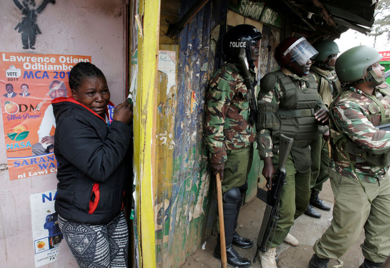 © Reuters. A woman cries as she stand behind policemen during clashes between supporter of opposition leader Raila Odinga and policemen in Kibera slum in Nairobi