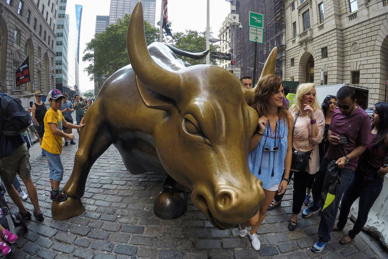 © Reuters. People pose next to the Wall Street Bull in the financial district in New York