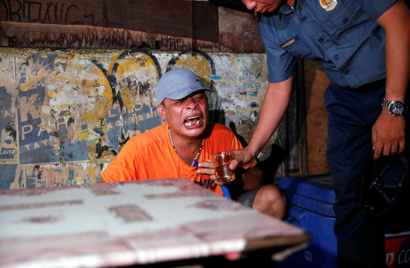 © Reuters. A police officer gives a glass of water to a man as he comforts him after his brother, who police say was killed in a spate of drug-related violence overnight, was shot in Manila