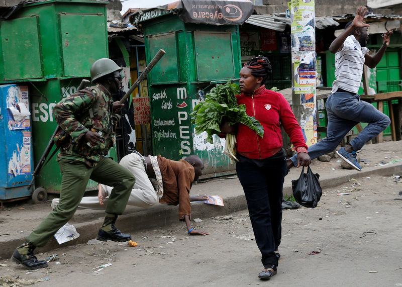 © Reuters. FILE PHOTO: An anti riot policeman attempts to disperse people from the street as a woman carrying vegetables walks past in Mathare, in Nairobi