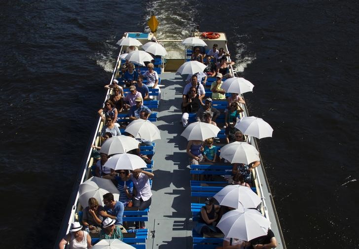 © Reuters. Tourists protect themselves from sun with umbrellas as they travel on river Spree sightseeing boat during hot summer day in Berlin