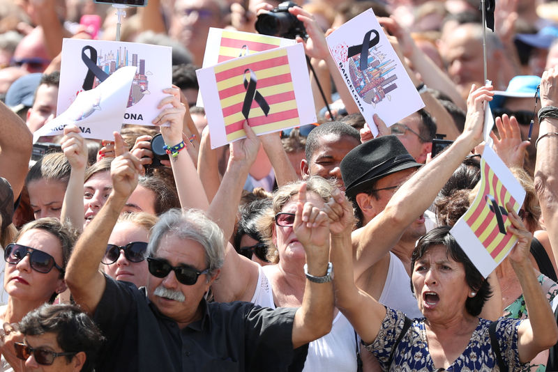 © Reuters. People hold banners as they observe a minute of silence in Placa de Catalunya, a day after a van crashed into pedestrians at Las Ramblas in Barcelona