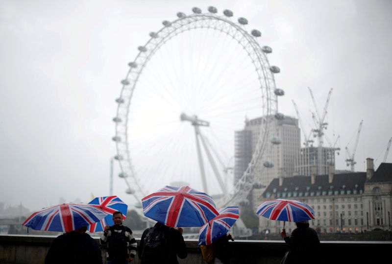 © Reuters. FILE PHOTO: Tourists carrying Union Flag umbrellas shelter from the rain in front of the London Eye wheel in London