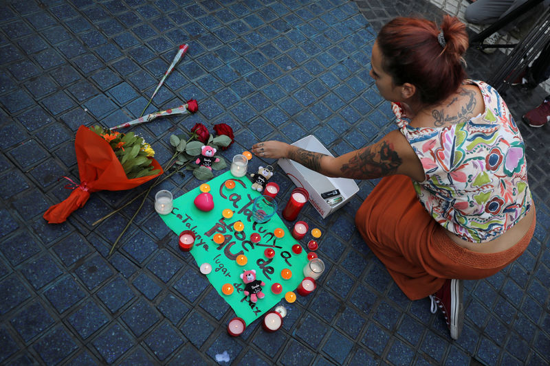 © Reuters. A woman places a candle on a placard, reading in Spanish and Catalan "Catalonia, place of peace", in the area where a van crashed into pedestrians at Las Ramblas street in Barcelona