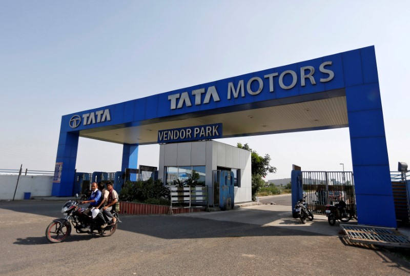 © Reuters. FILE PHOTO: Men ride a motorbike past a Tata Motors car plant at Sanand