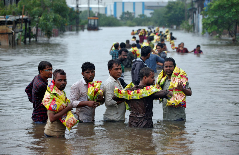 © Reuters. People carry packets of snacks after receiving them from civil defence volunteers in a flooded neighbourhood after heavy rains in Ahmedabad