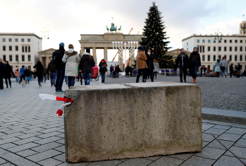 © Reuters. FILE PHOTO: People walk beside a concrete barrier at the Brandenburg Gate ahead of the upcoming New Year's Eve celebrations in Berlin