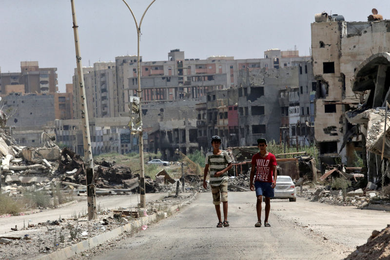 © Reuters. Men walk near destroyed buildings in Sabri, a central Benghazi district