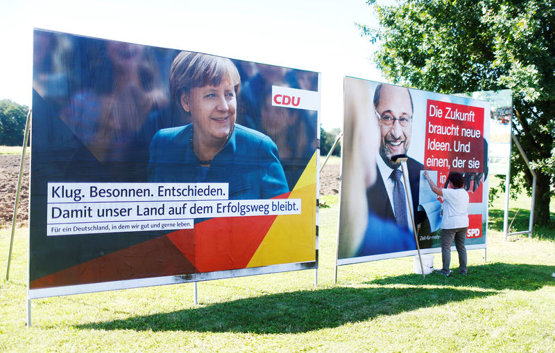 © Reuters. A woman glues poster of the two top candidates for the upcoming general elections, German Chancellor Merkel for the Christian Democratic Union party (CDU), and Schulz for Social Democratic Party (SPD) before an election campaign rally in Bitterfeld-Wolfen