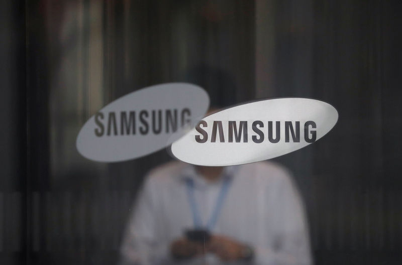 © Reuters. FILE PHOTO - An employee using his mobile phone walks past the logo of Samsung Electronics at its office building in Seoul