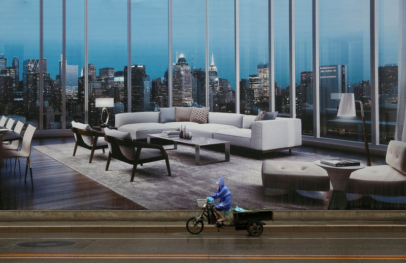 © Reuters. FILE PHOTO: A man rides a tricycle past an advertising poster for luxury apartments in Beijing,